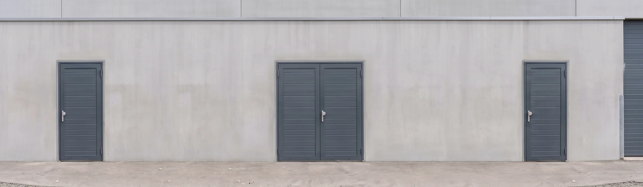 Grijze aluminium loopdeuren in een witte muur van een industrieel gebouw.