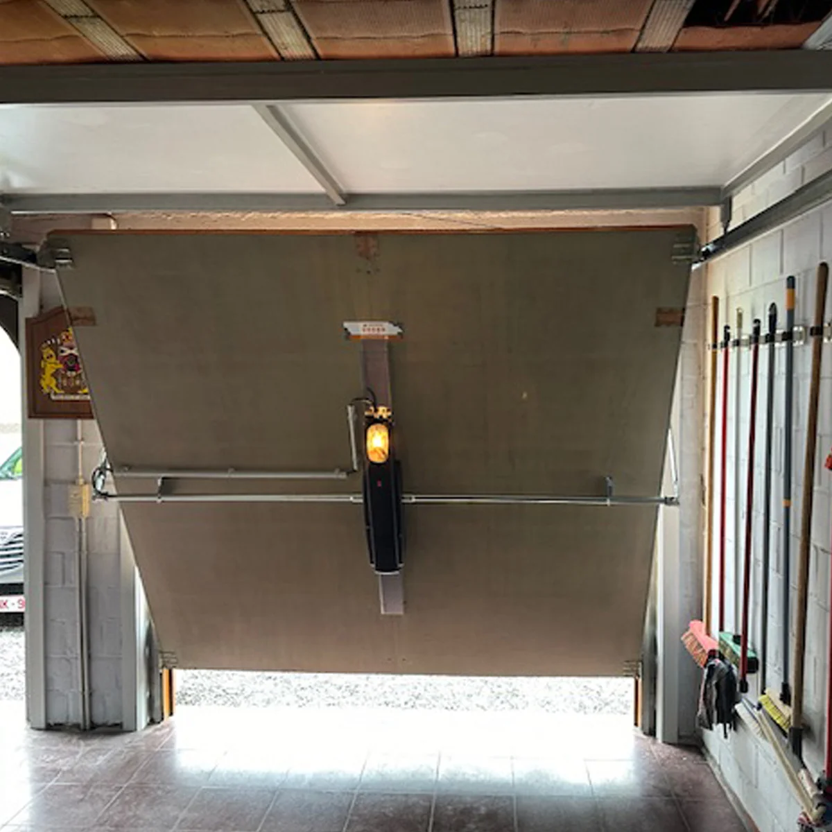 Garagedeur met elektrische opener en sensoren, geflankeerd door opbergruimte met gereedschappen en materialen.