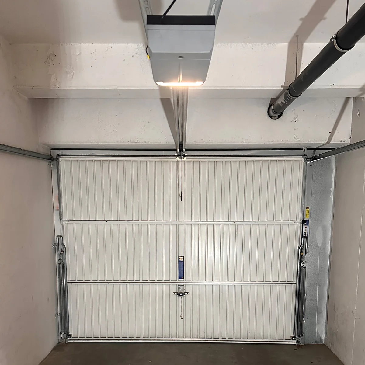 Witte sectionaaldeur van een garage met horizontale profielen, openers en een LED-verlichting aan het plafond.