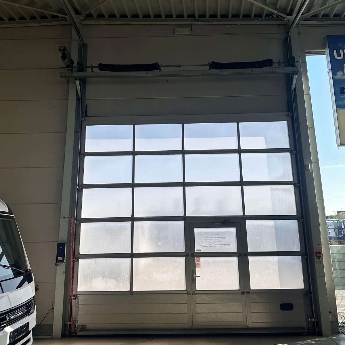 Moderne garagedeur met gedeeltelijk transparante panelen in een grijze aluminium constructie met zwarte indeling in rijen.