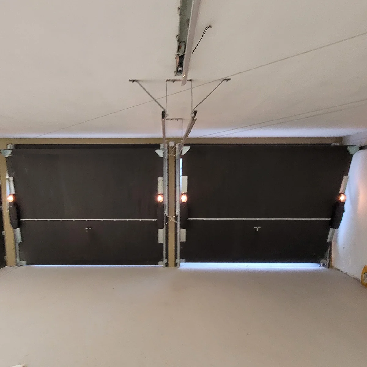 Twee zwarte garagepoorten met geïntegreerde LED-verlichting in een witte garagewand met metalen framewerk.