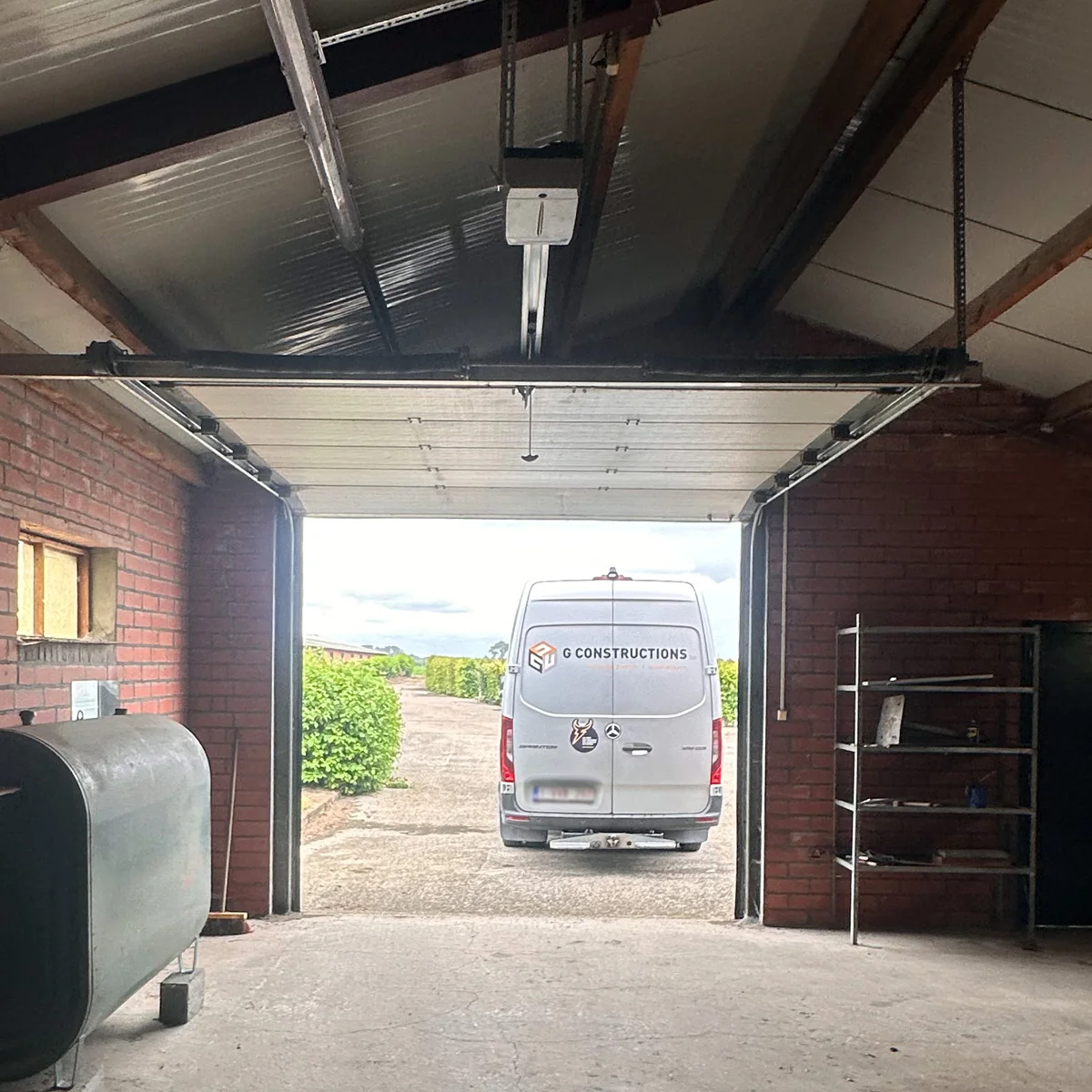 Geopende aluminium garagepoort in een bakstenen garage met zicht op een witte bestelwagen buiten.