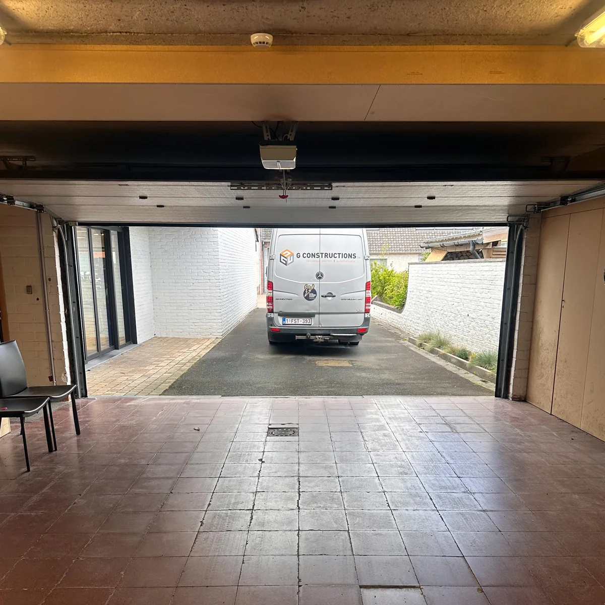 Geopende garagedeur met zicht op een witte bedrijfsbus in een verharde oprit buiten.