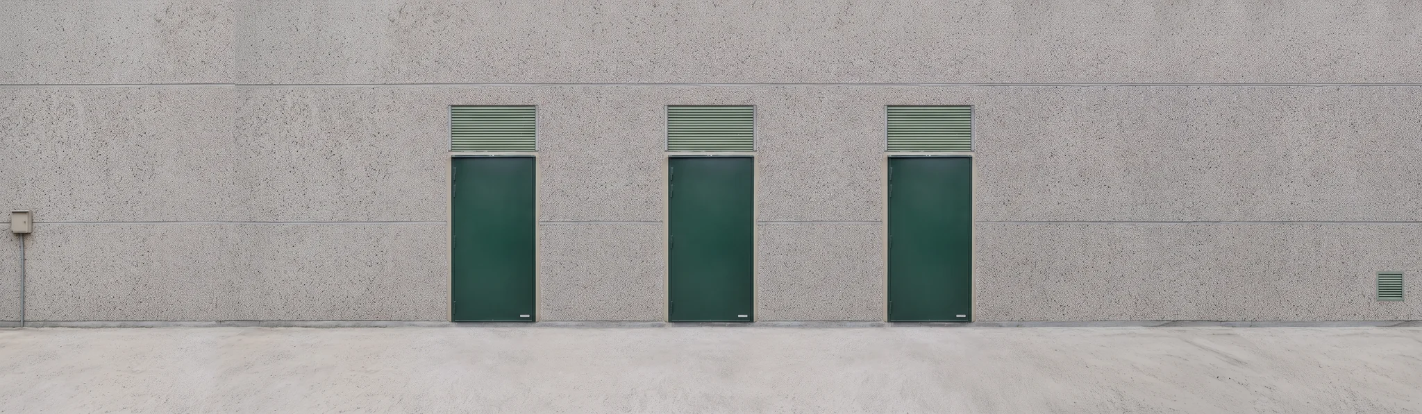 Drie groen gekleurde branddeuren met licht bovenramen in een grijze betonnen gevel.