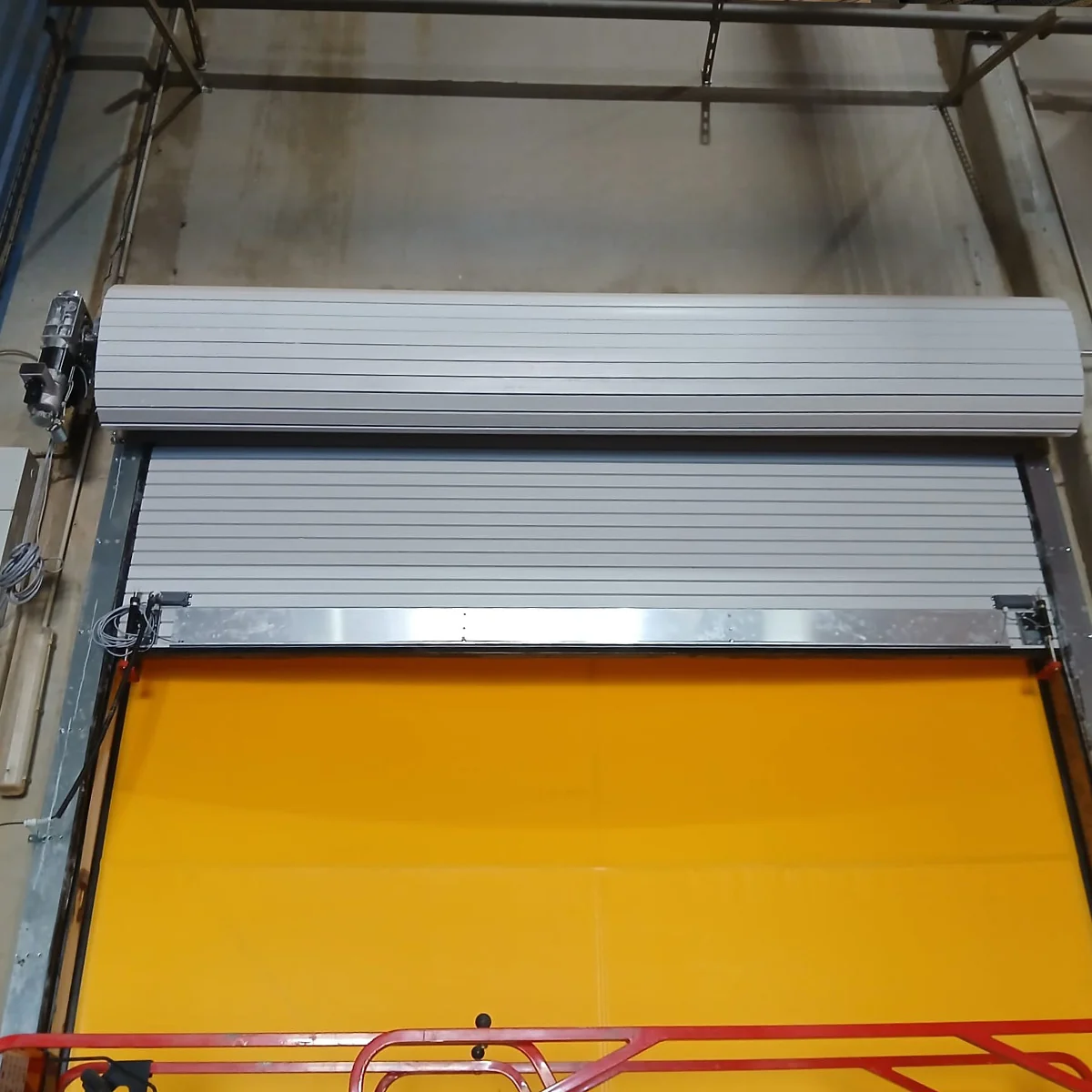 Twee gesloten aluminium brandwerende roldeuren met horizontale latten boven een gele laadklep.