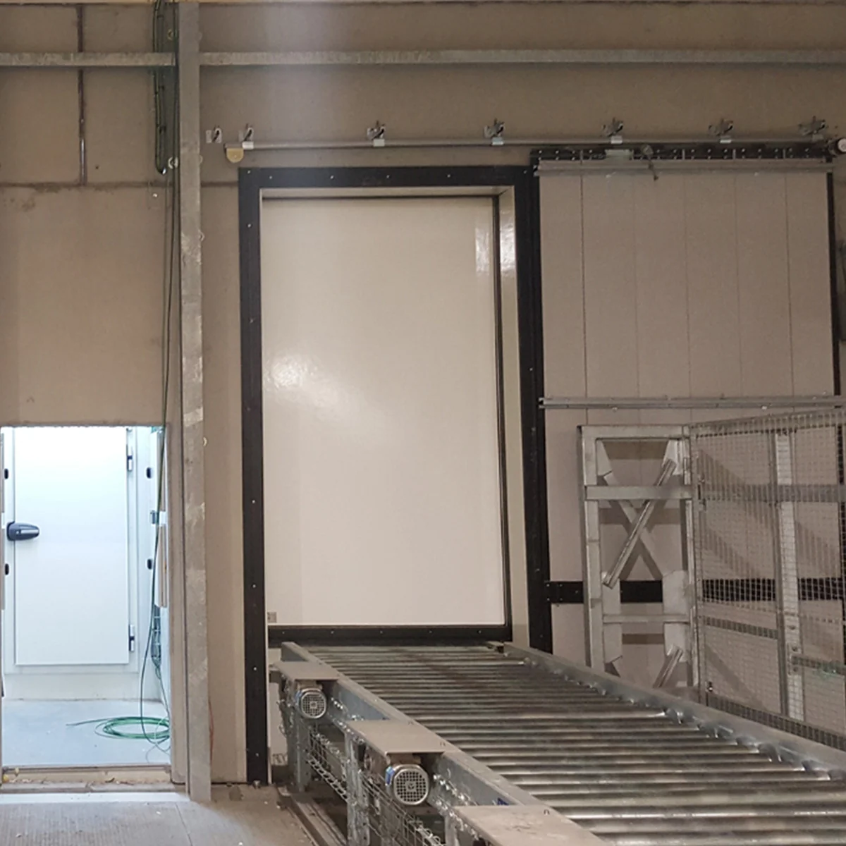 Schuifpoort met zwart frame en brandwerend paneel in industriële ruimte met metalen rollers.