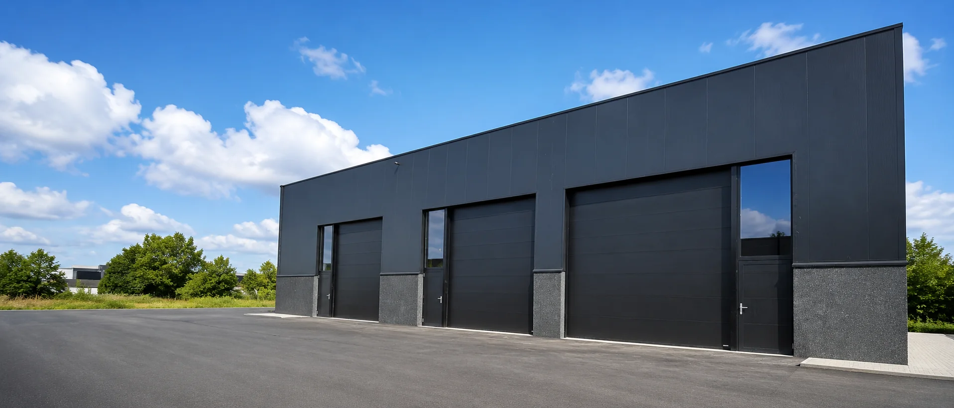Modern industrieel gebouw met drie zwarte sectionaalpoorten en grijze sokkel aan de voorgevel.