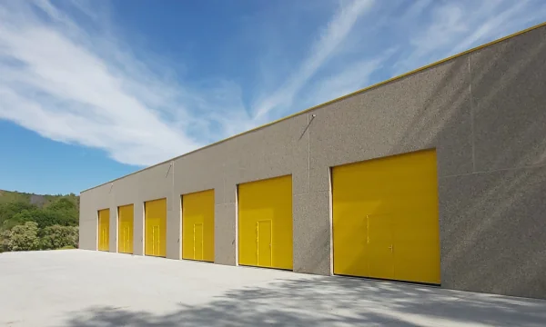Moderne betonnen garage met vijf grote gele deuren onder blauwe hemel.