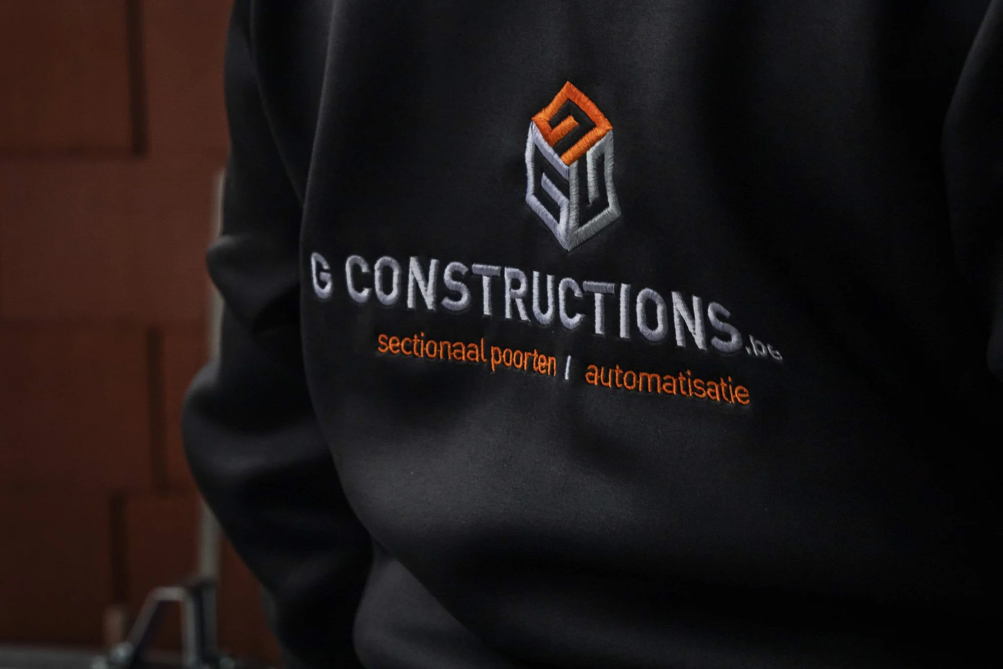 Zwart sweatshirt met geborduurd logo en tekst van G Constructions met vermelding van sectionaal poorten en automatisatie.