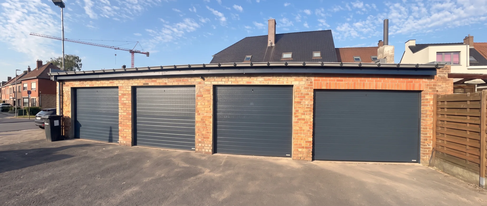 Modern bakstenen garagebouw met vier grijze automatische garagepoortenin een woonwijk.
