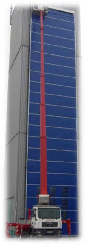 Een witte vrachtwagen met rode uitschuifbare mast tegen een groot blauw zonnepaneelgebouw geplaatst.