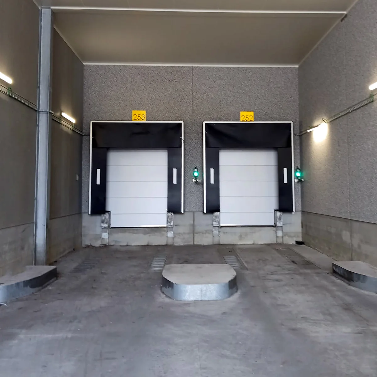 Twee witte laaddeuren met zwarte omlijsting in een betonnen laadkuil, elk gemarkeerd met een geel nummerbord.