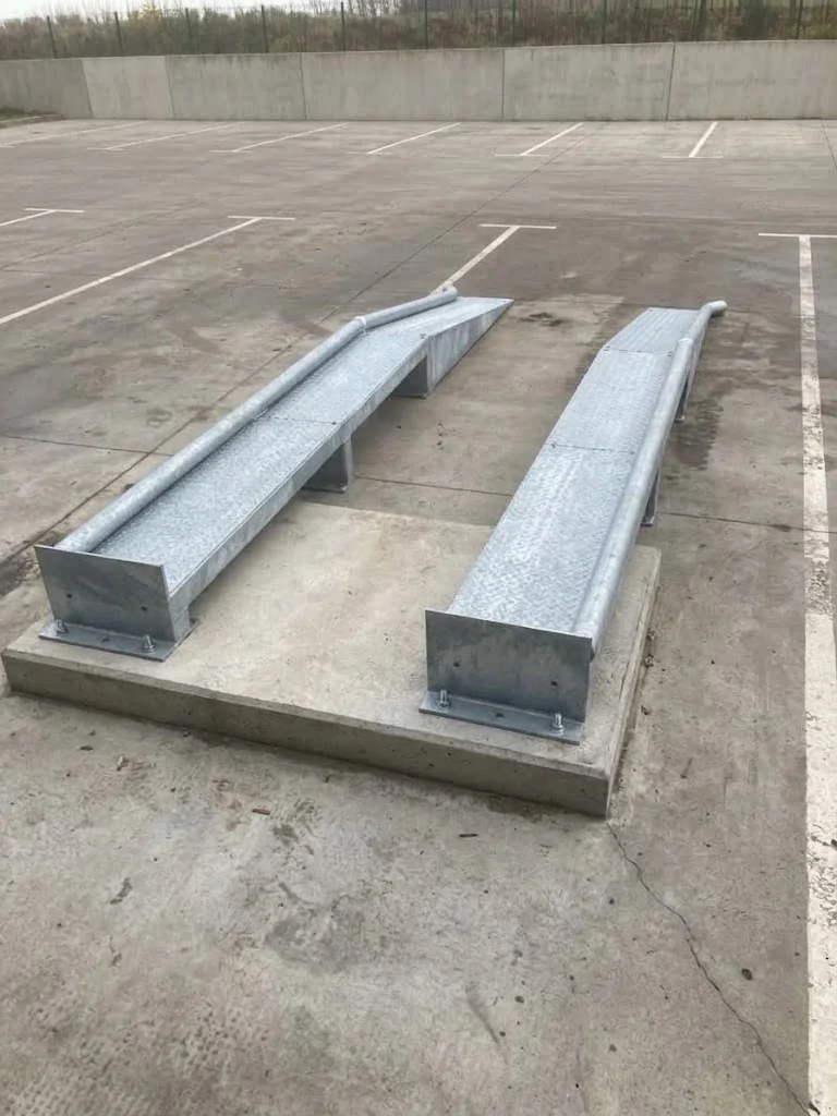 Twee gegalvaniseerde metalen ophogers op een betonnen ondergrond in een parkeergarage met witte parkeervakken.