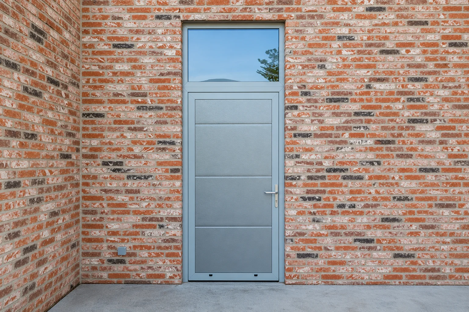 Grijze aluminium loopdeuren met glas bovenlicht in rode bakstenen muur met uitzicht op water en bomen.