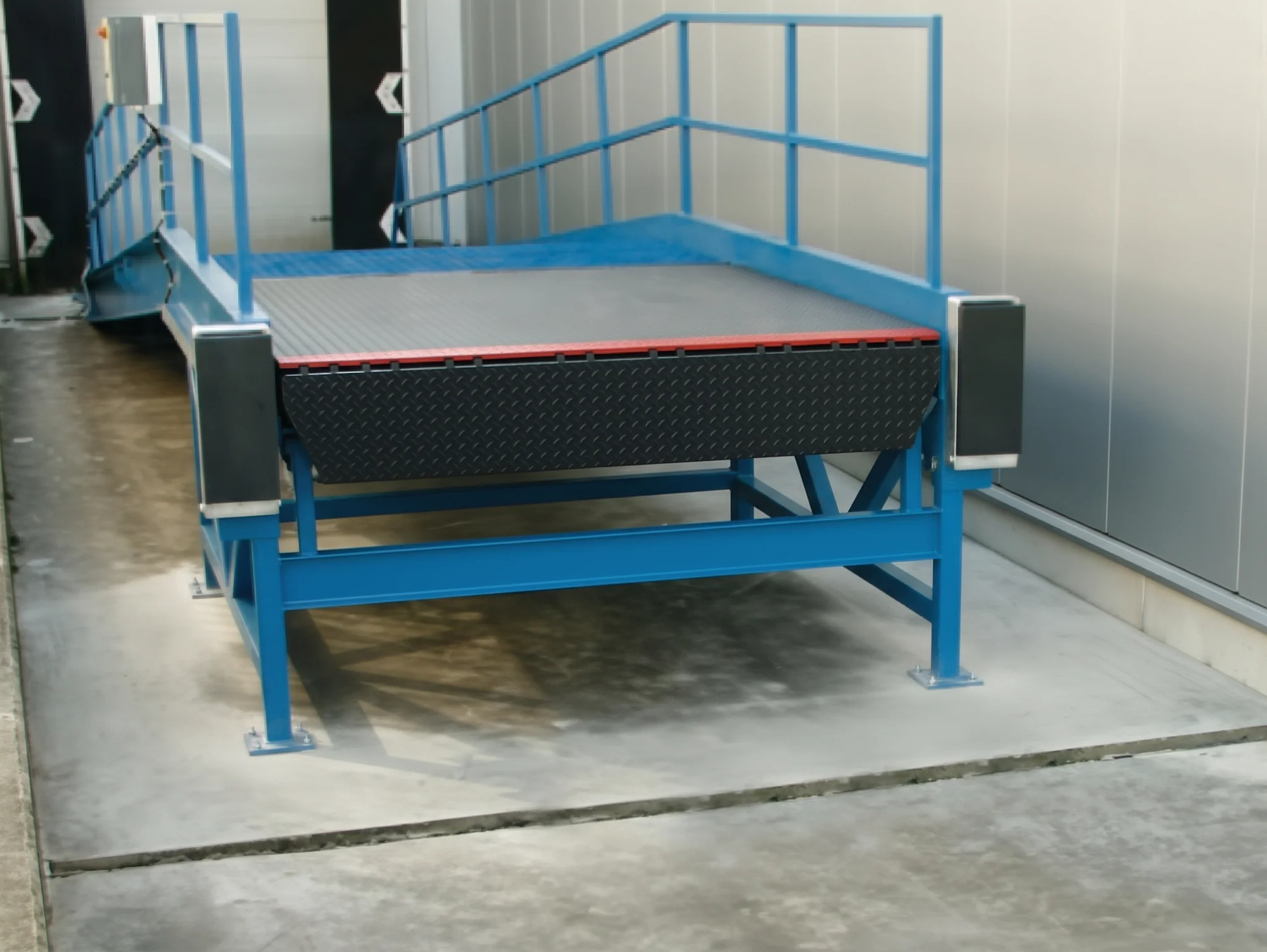 Industriële laadram met blauwe stalen frame en grijze oprijplaat met rubberen rand, voorzien van zijbehuizing.