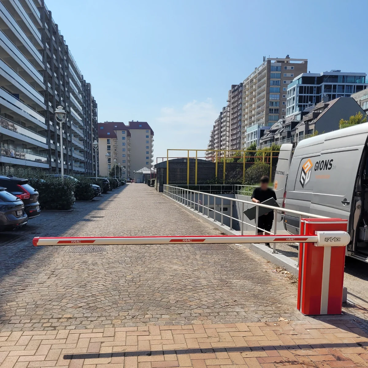 Rood-witte slagboom met gele palen in een parkeergarage tussen moderne appartementengebouwen.