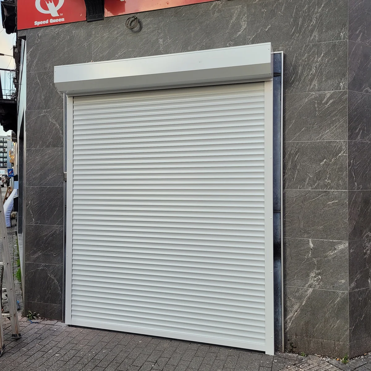 Gesloten witte roldeur op een gevel met donkergrijze tegels.