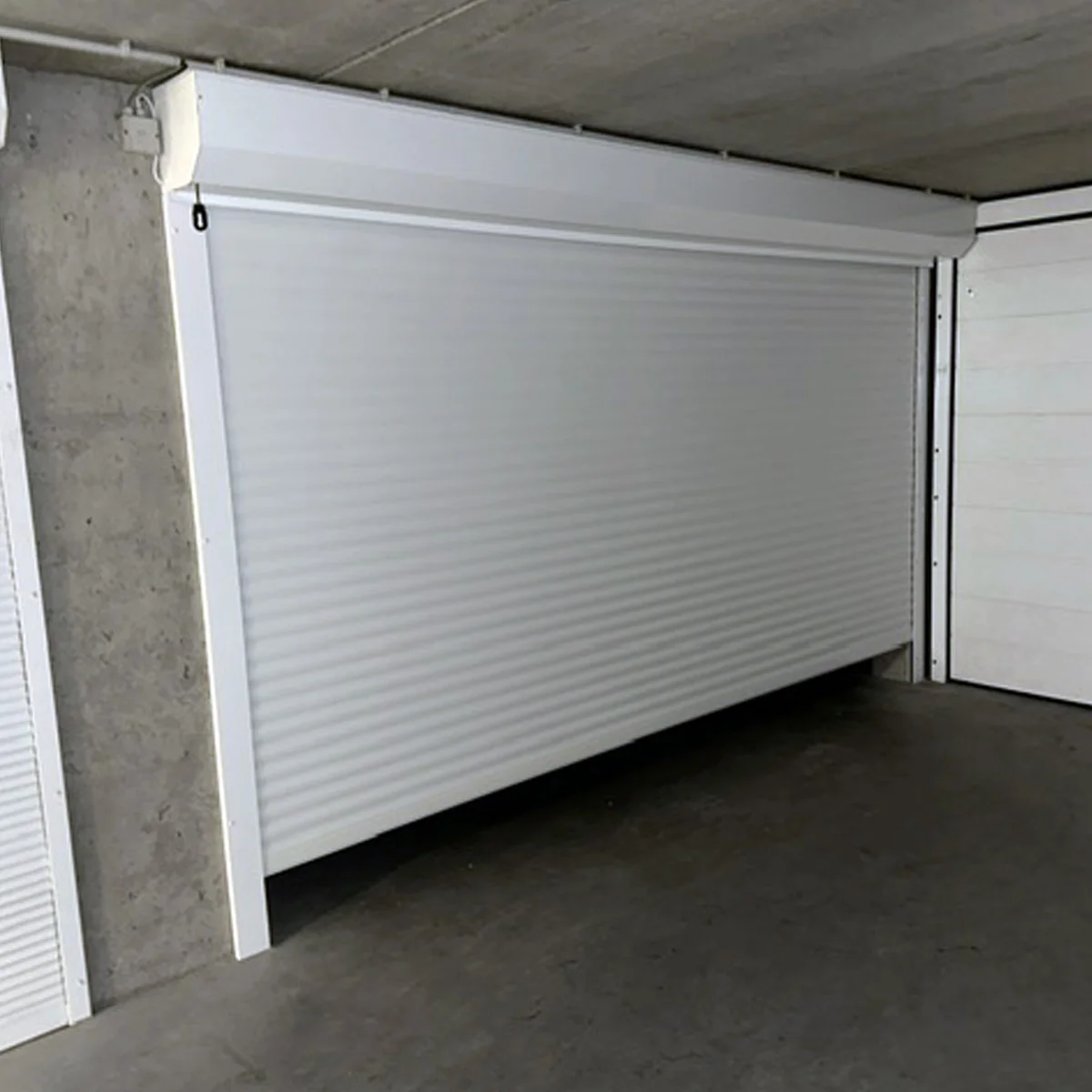 Witte aluminium rolpoorten in een gesloten positie in een betonnen garage of opslagruimte.
