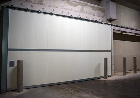 Grote witte garagedeur met horizontale verdeling en donkere raamstroken in een industriële ruimte.
