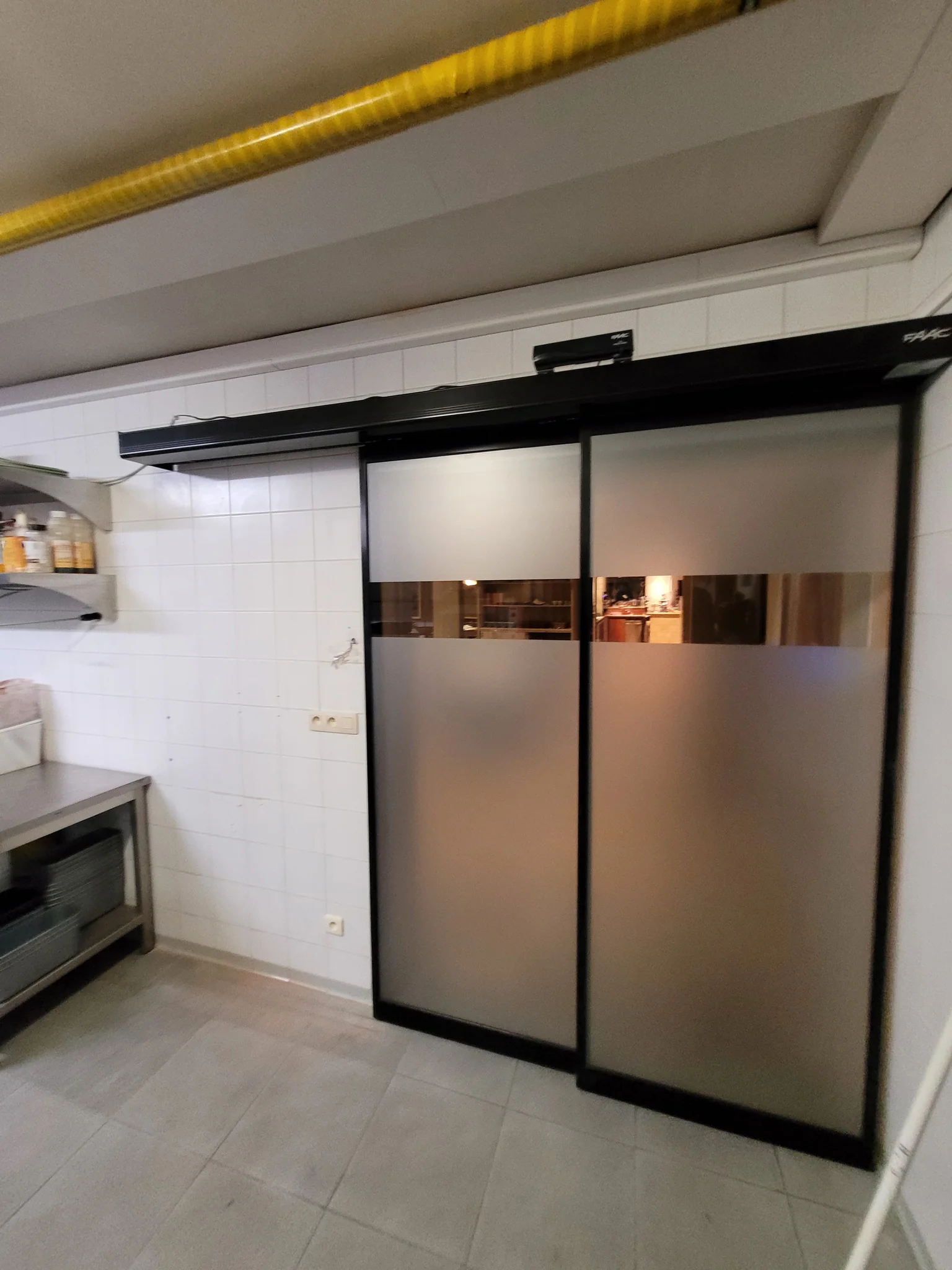 Moderne schuifdeuren met zwart frame en matglazen panelen in een keuken met witte tegels.