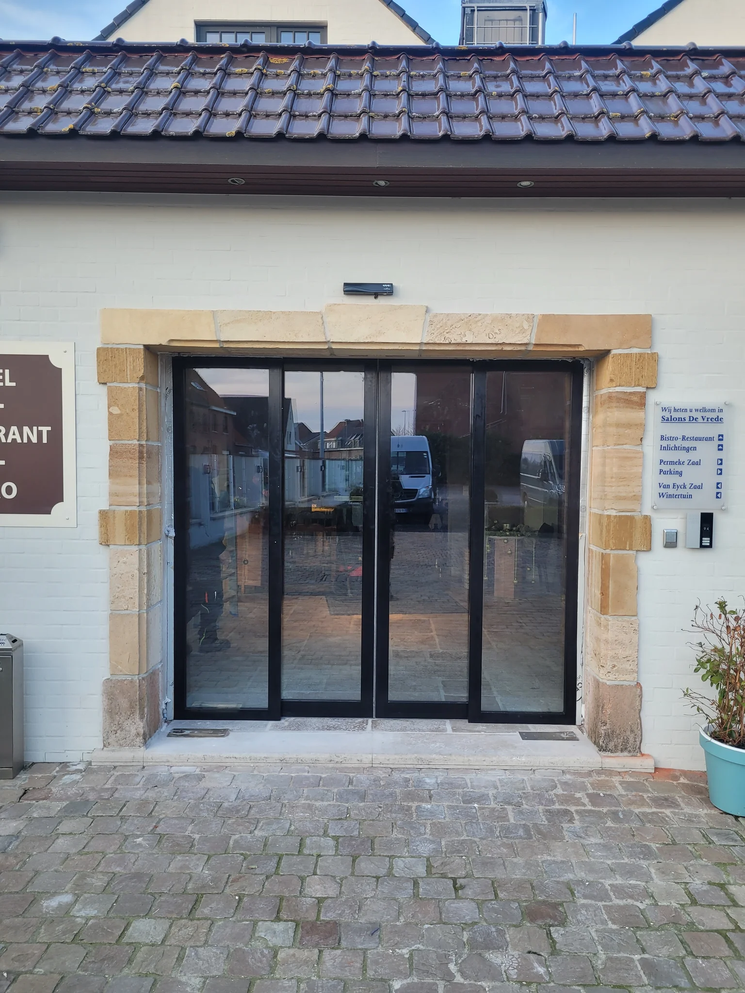 Glazen schuifdeuren met zwarte aluminium profielen en zandstenen omlijsting aan de voorgevel van een gebouw met pannendak.