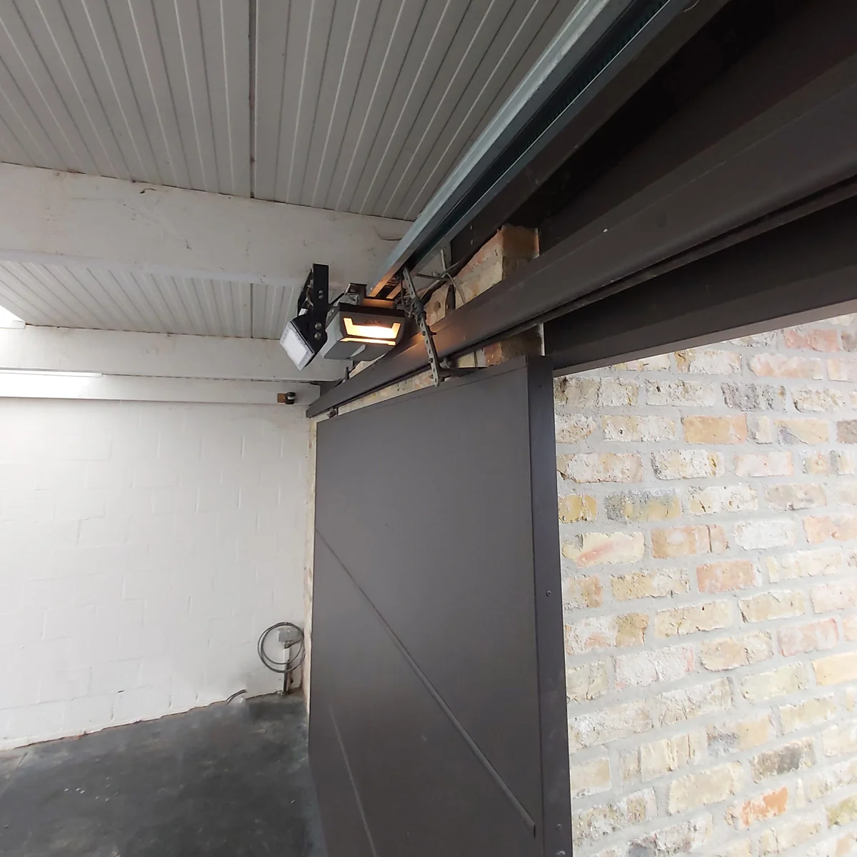 Interieur van een garage met een grijze schuifdeur en een bewegingssensor aan het plafond boven de deur.
