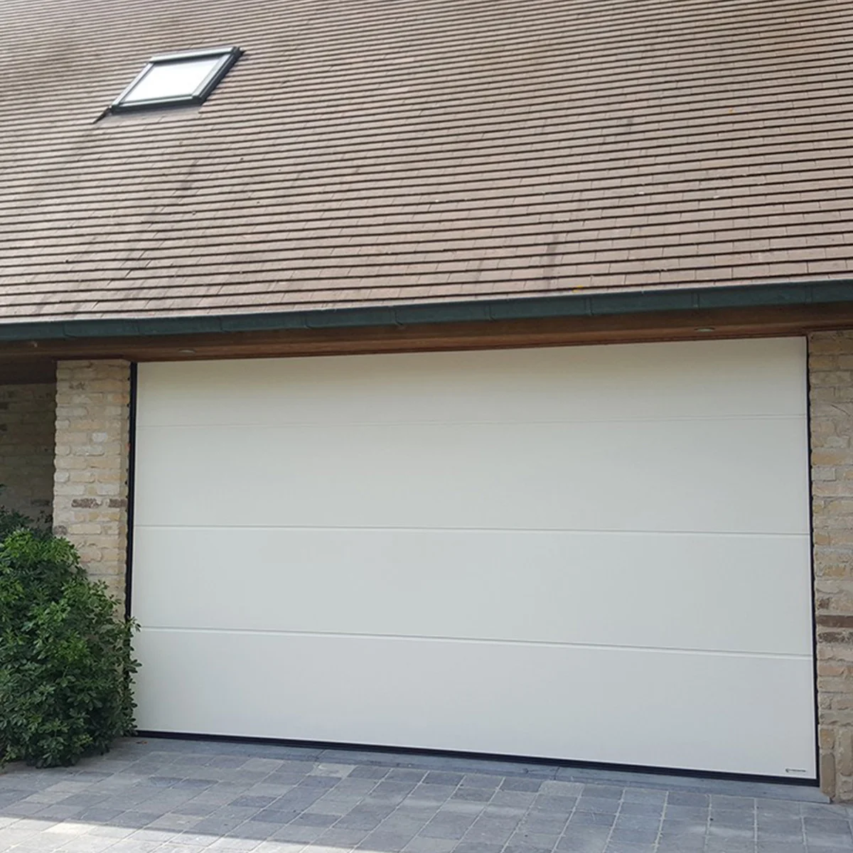 Moderne witte sectionaalpoort met horizontale paneelindeling aan voorzijde van een woning met grijze leisteen dak.