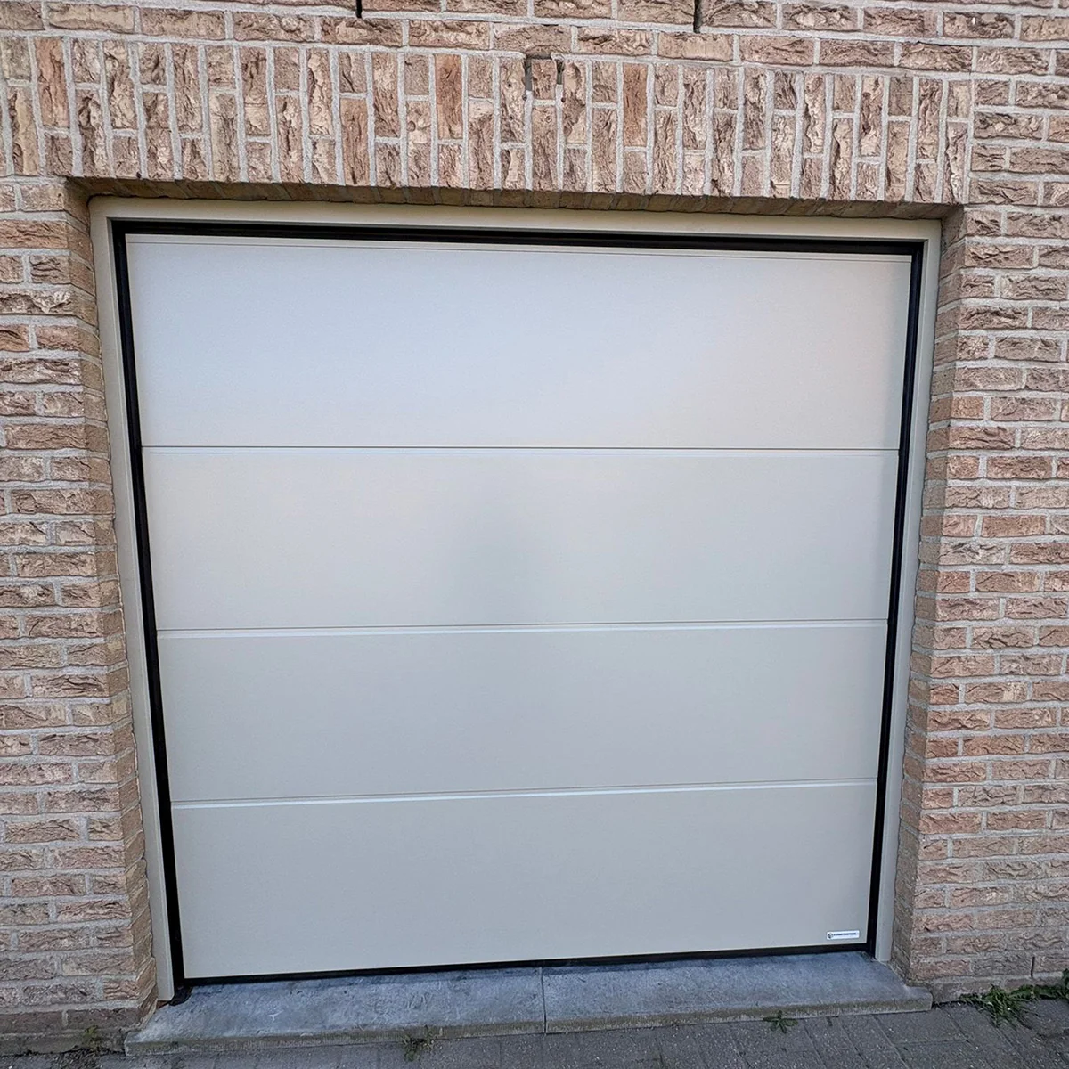 Witte sectionaaldeur met horizontale panelen in zwart frame, ingebouwd in bakstenen gevel van een garage.