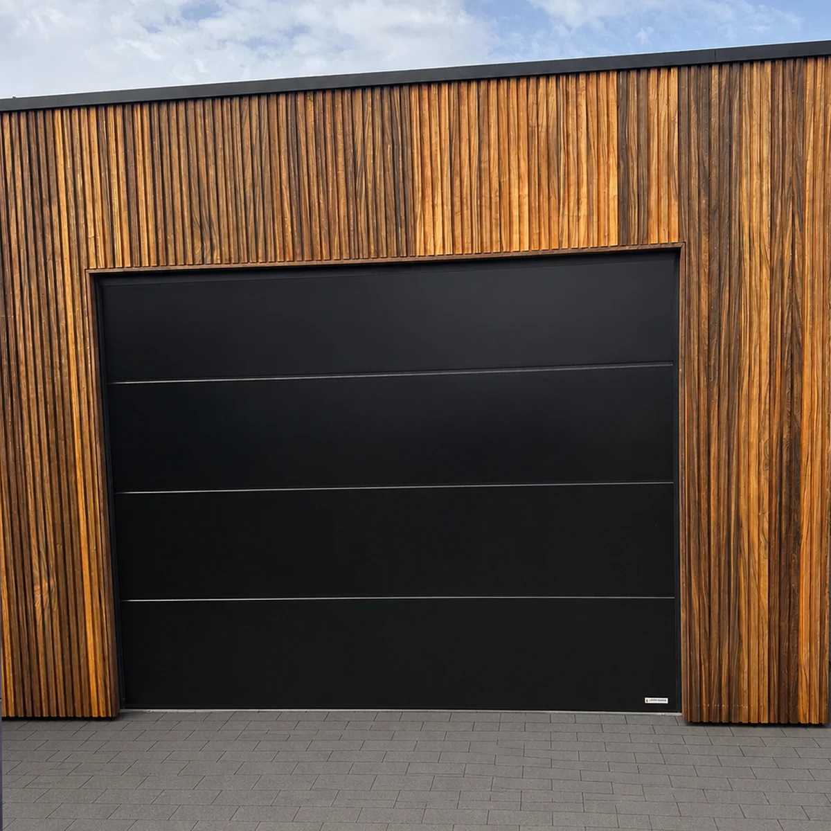 Moderne garagedeur met zwarte sectionaalpanelen in houten gevelbekleding met verticale lijnen.