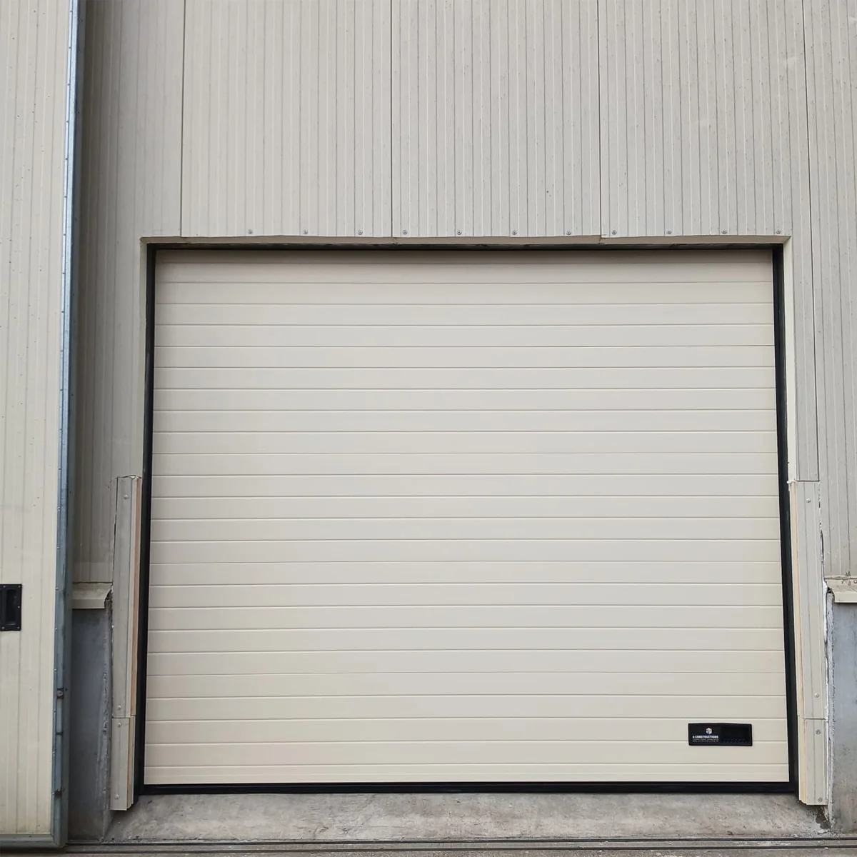 Beige sectionaaldeur met horizontale latten en zwart frame in industriële grijze wand ingebouwd.