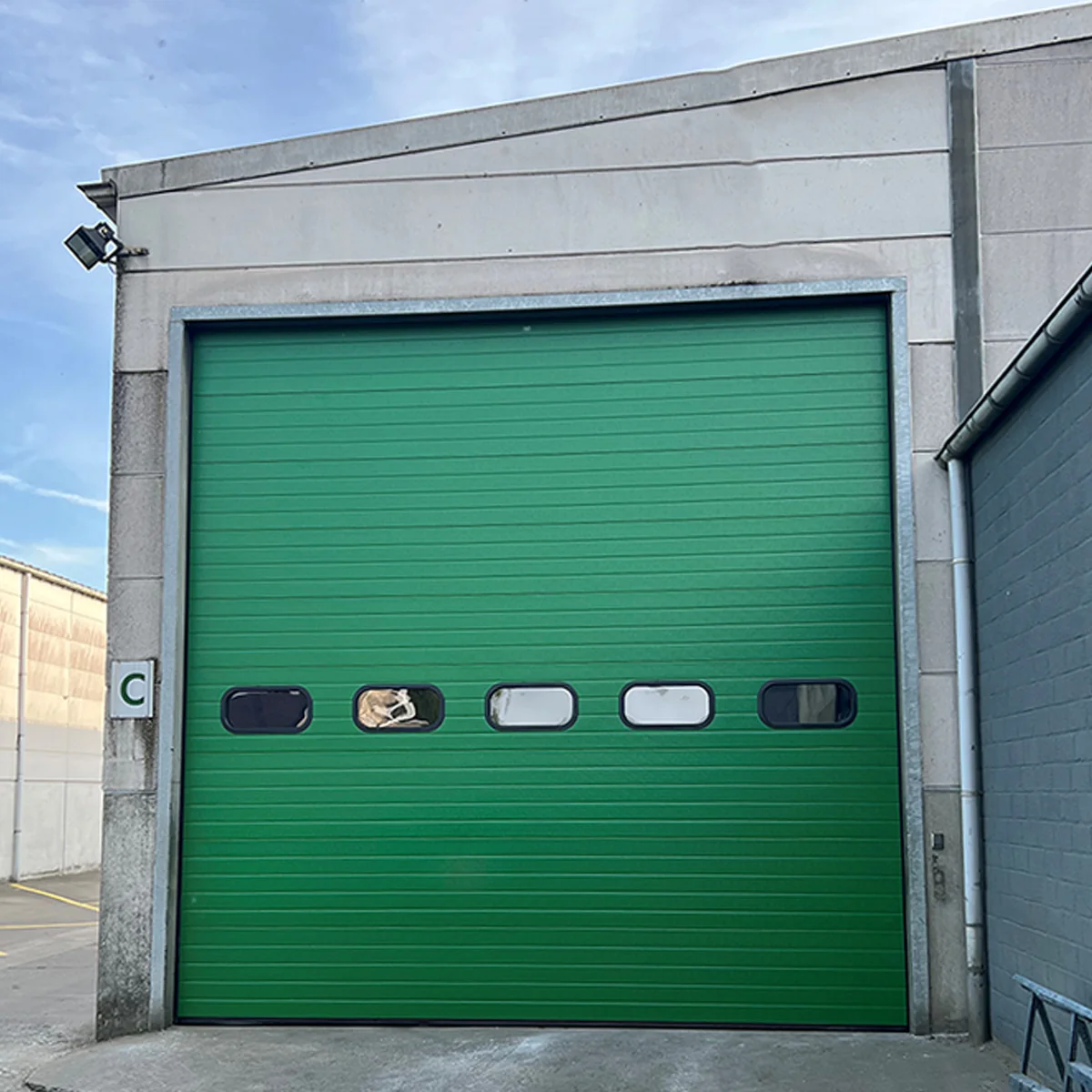 Industriële sectionaalpoort in groen met vijf ramen, gemonteerd in betonnen kozijn op een bedrijfsgebouw.