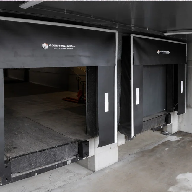 Twee zwarte dockshelters met witte zijkanten en opgestelde laaddeuren aan een betonnen laadperron in aanbouw.