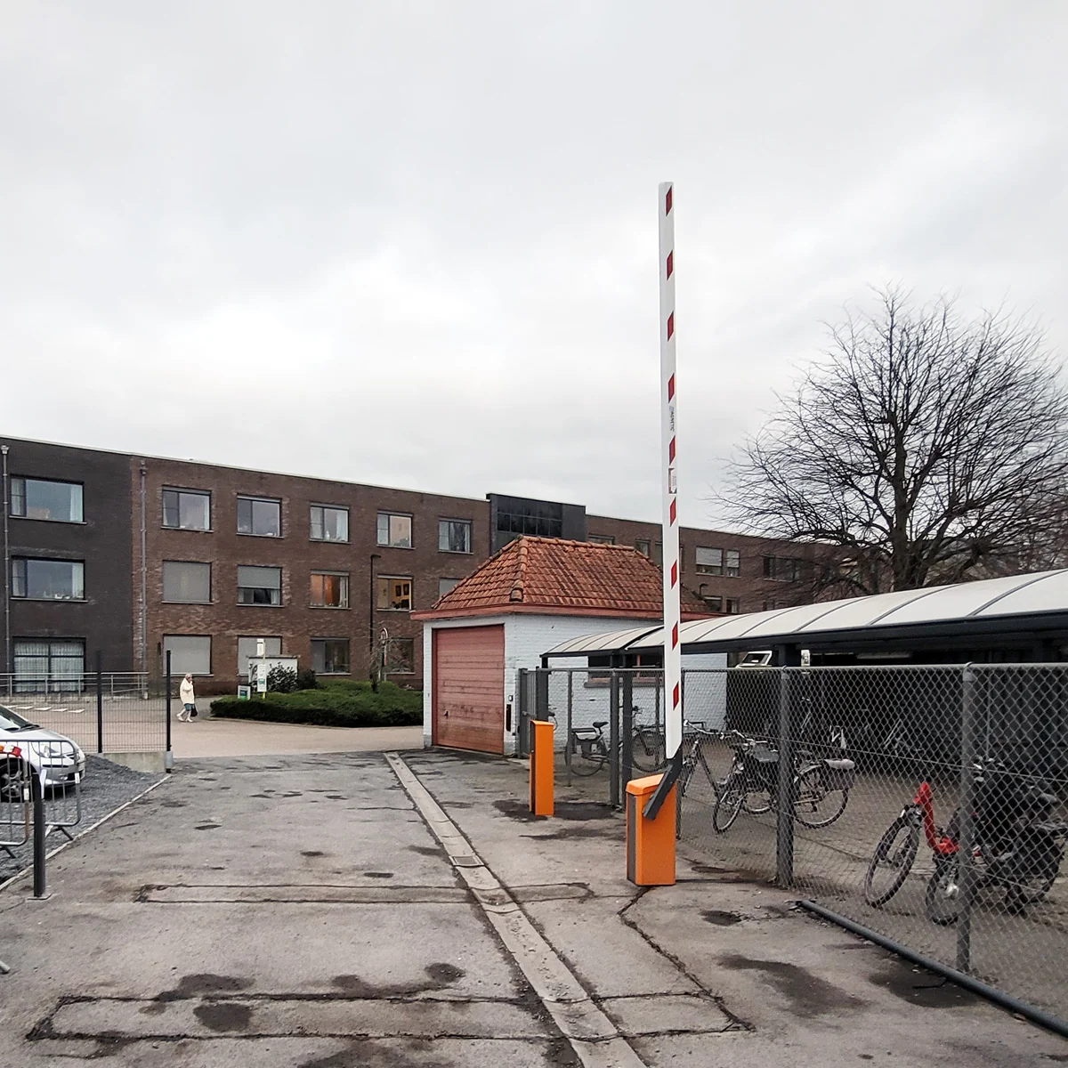 Parkeerterrein met een witte en rode gestreepte slagboom, oranje palen en een fietsenstalling met fietsen achter gaas.