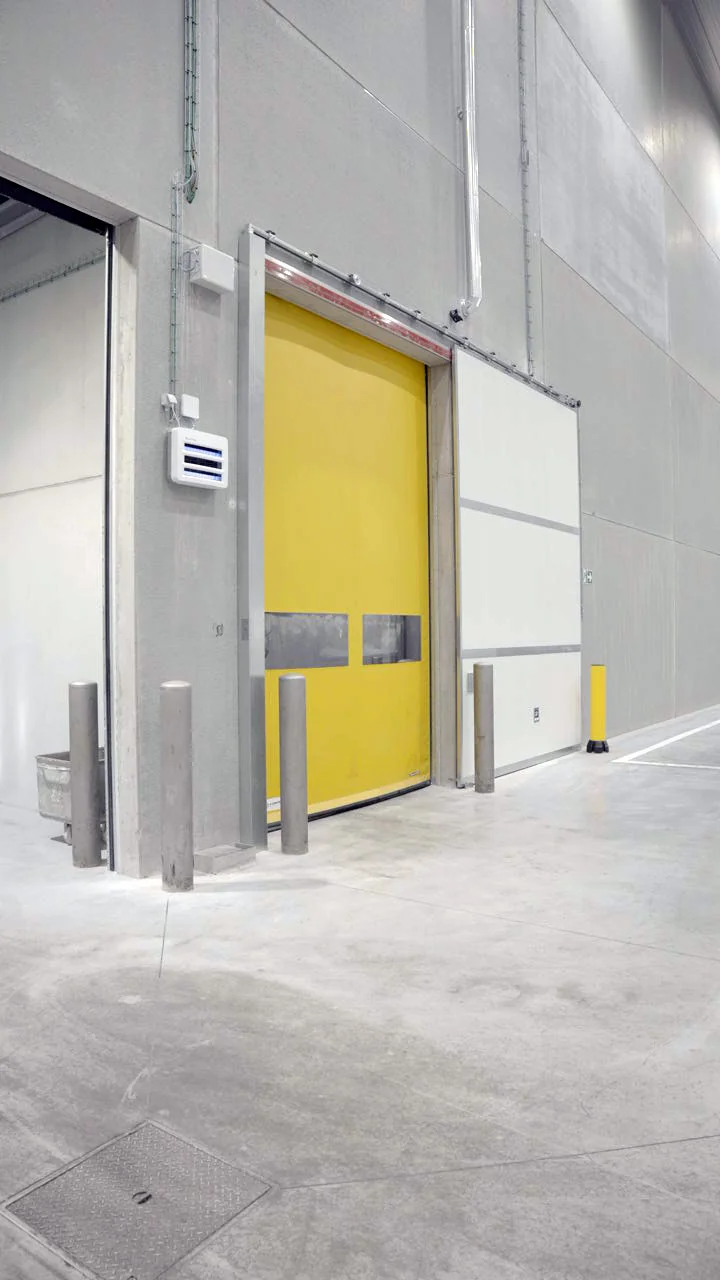 Industriële laadruimte met gele vouwdeur, betonnen muren, grijze posten en witte zijdeuren in moderne fabriek.