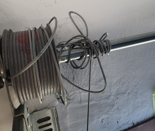 Opgerolde staalkabel op een poortmechanisme met verstrengelde en losse kabeleinden zichtbaar.