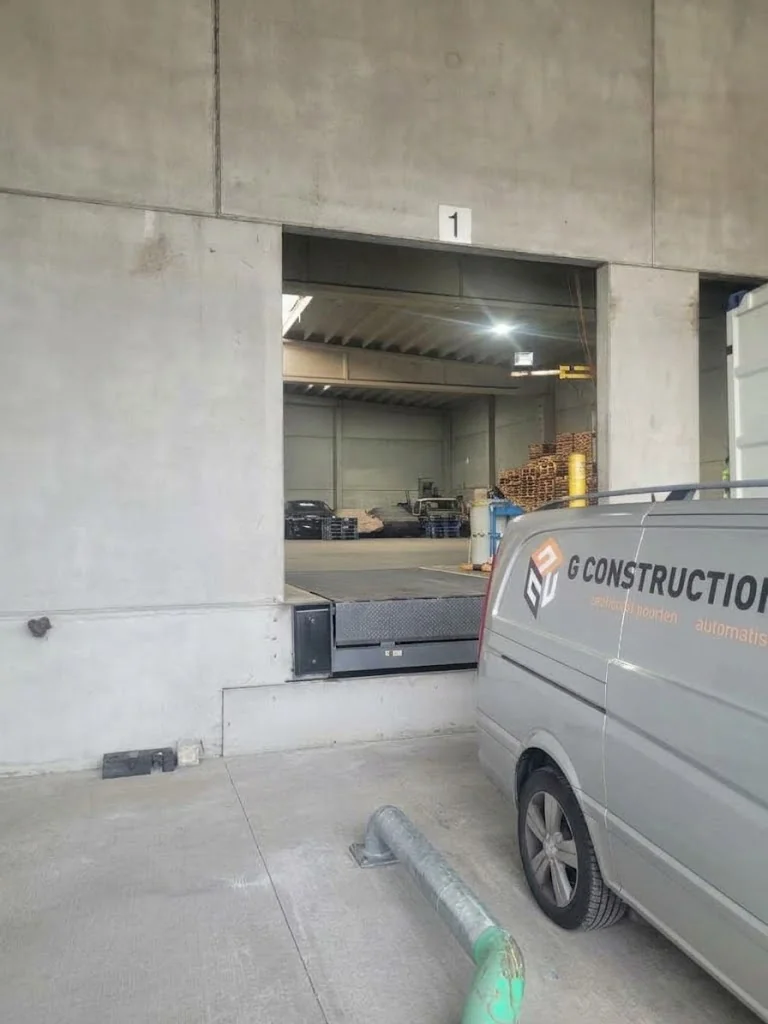Grijze bestelbus van G Construction geparkeerd voor open garageruimte nummer 1 met betonnen muren.