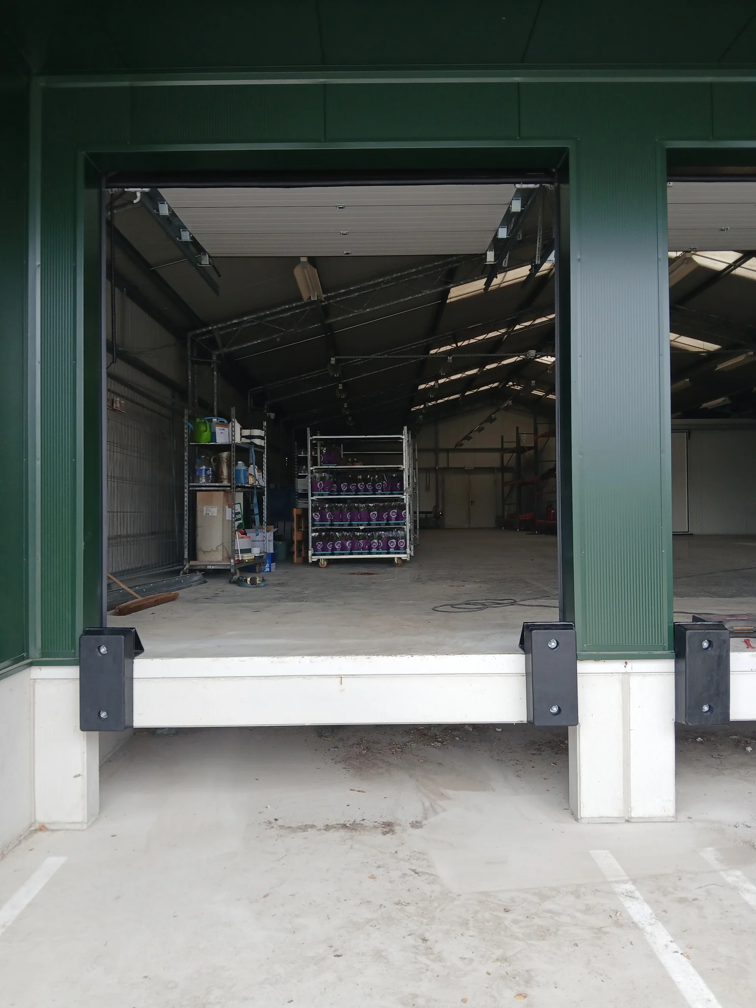 Witte en zwarte stootbuffers bevestigd onder de laadklep van een groen magazijngebouw.