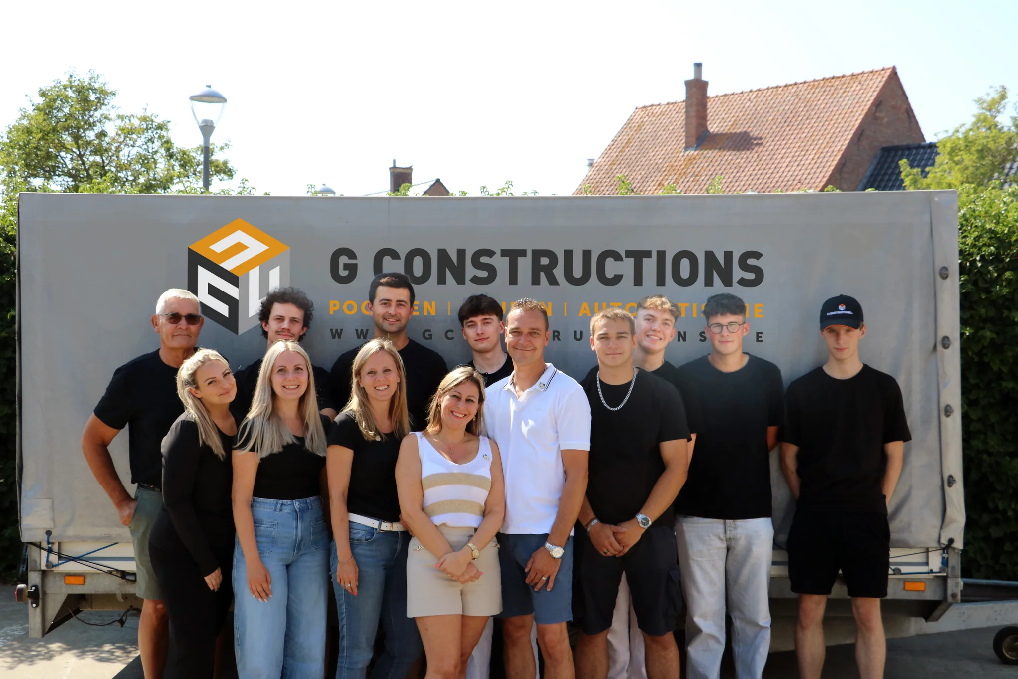 Een groep van twaalf personen staat voor een vrachtwagen met het G Constructions logo en bedrijfsnaam erop afgedrukt.