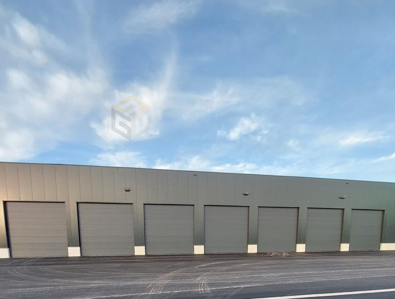 Industrieel gebouw met zeven grijze sectionaalpoorten naast elkaar onder blauwe bewolkte hemel.