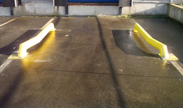 Twee gele polyurethaan geleiders op een parkeerplaats met twee brede groeven, voorzien van reflecterende witte strepen voor verkeersveiligheid.