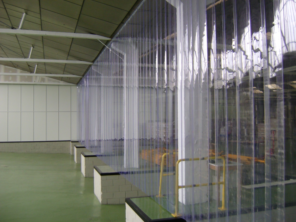 Industriële ruimte met transparante brandwerende scheidingswanden van kunststof en geel veiligheidshekwerk.
