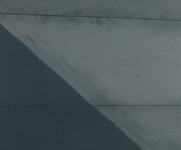 Gesloten grijze garagedeur met horizontale panelen en schaduw door zonlicht, waarop vuil en stof zichtbaar zijn.