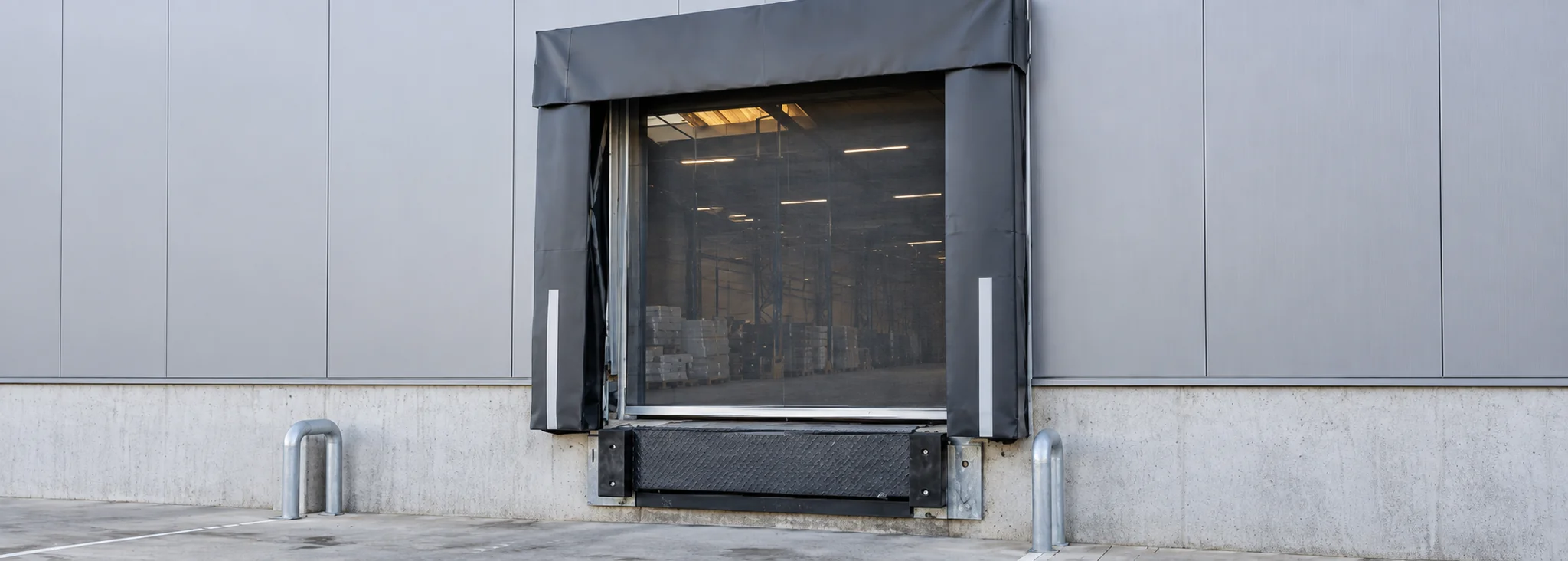 Industriële laadpoort met grijs canvas zijschermen en zwart vliegengaas voor vrachtwagenverlading aan betonnen gevel.